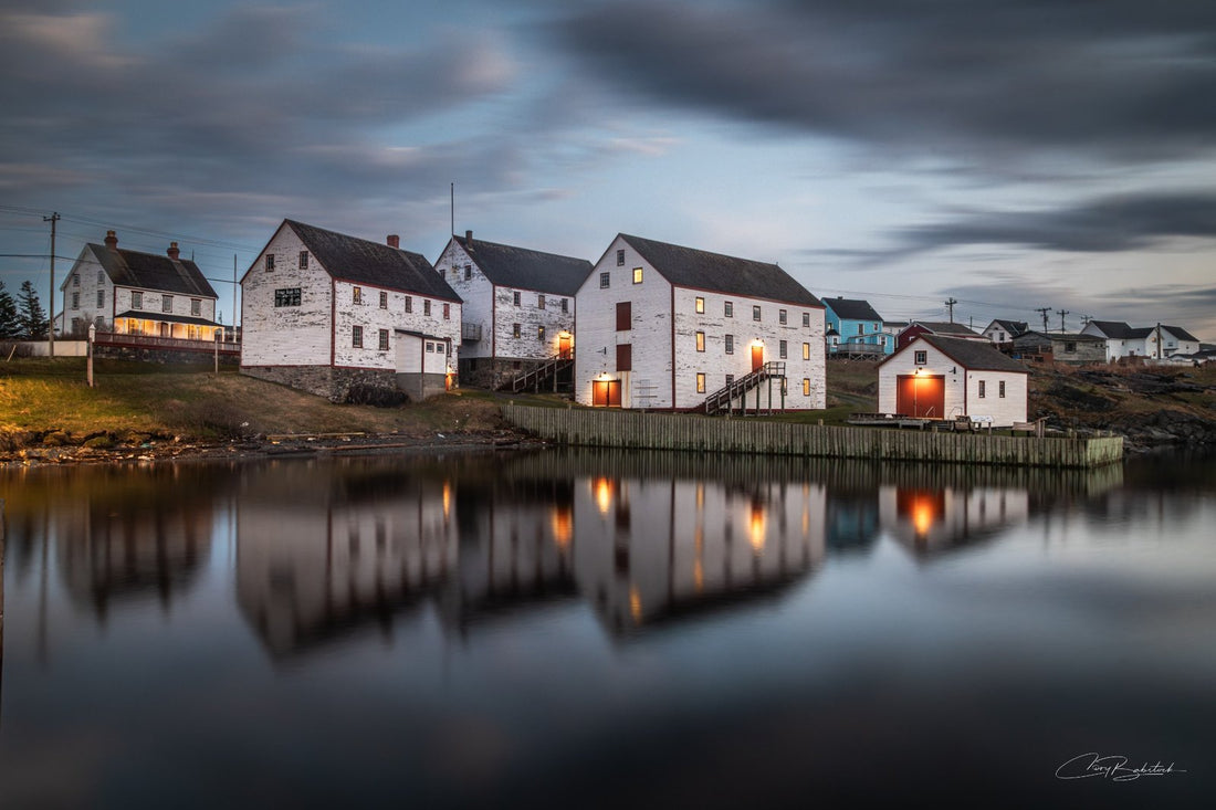 Historic Ryan Premises building illuminated at blue hour in Bonavista Newfoundland with reflections shimmering across calm harbour water under a cloudy evening sky