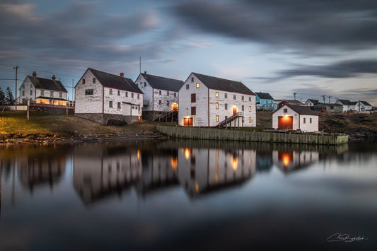 Historic Ryan Premises building illuminated at blue hour in Bonavista Newfoundland with reflections shimmering across calm harbour water under a cloudy evening sky